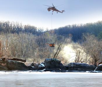 A helicopter lowers a drill rig to workers on the Potomac River.