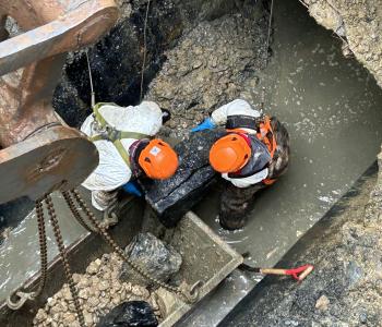 workers removing a large boulder in damaged pipe