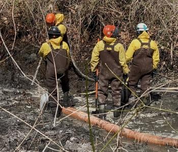 workers spraying and mucking sludge from canal