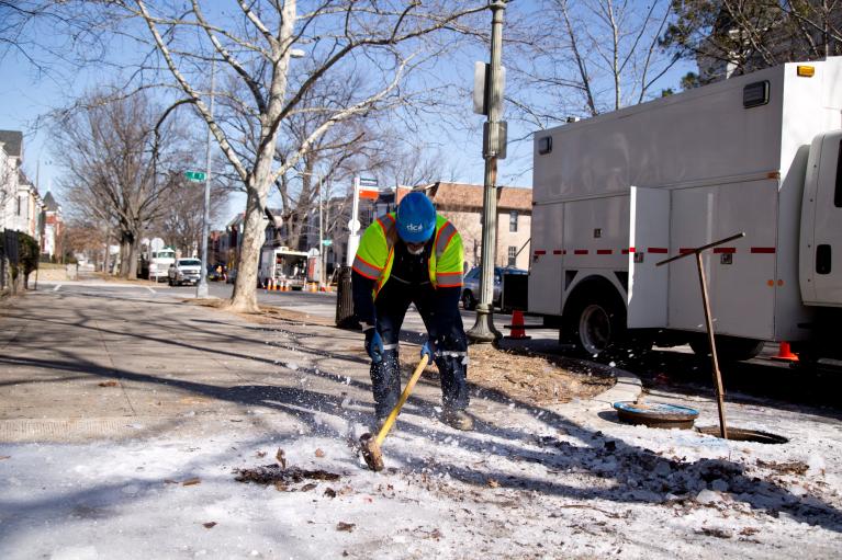 A DC Water employee breaks up ice on a sidewalk