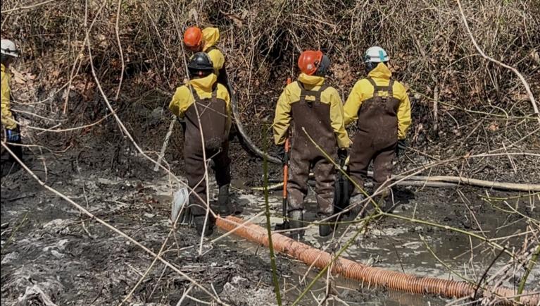 workers spraying and mucking sludge from canal