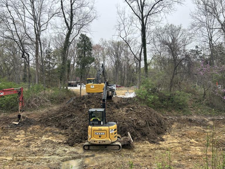 Excavators in the canal digging up soil and another excavator removing the soil to a dump truck to be hauled away 
