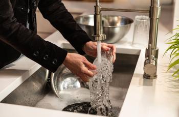 Photo shows an adult washing a glass in the sink with the faucet running.